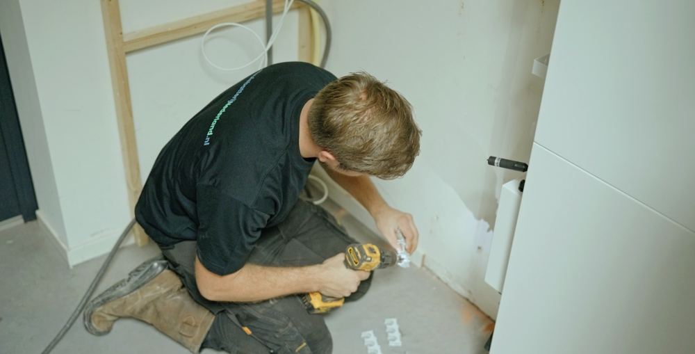 Monteur boort de muurbeugel voor de thuisbatterij vast